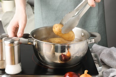 Woman putting raw potato into pot on stove, closeup