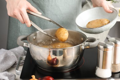 Photo of Woman putting raw potato into pot on stove, closeup