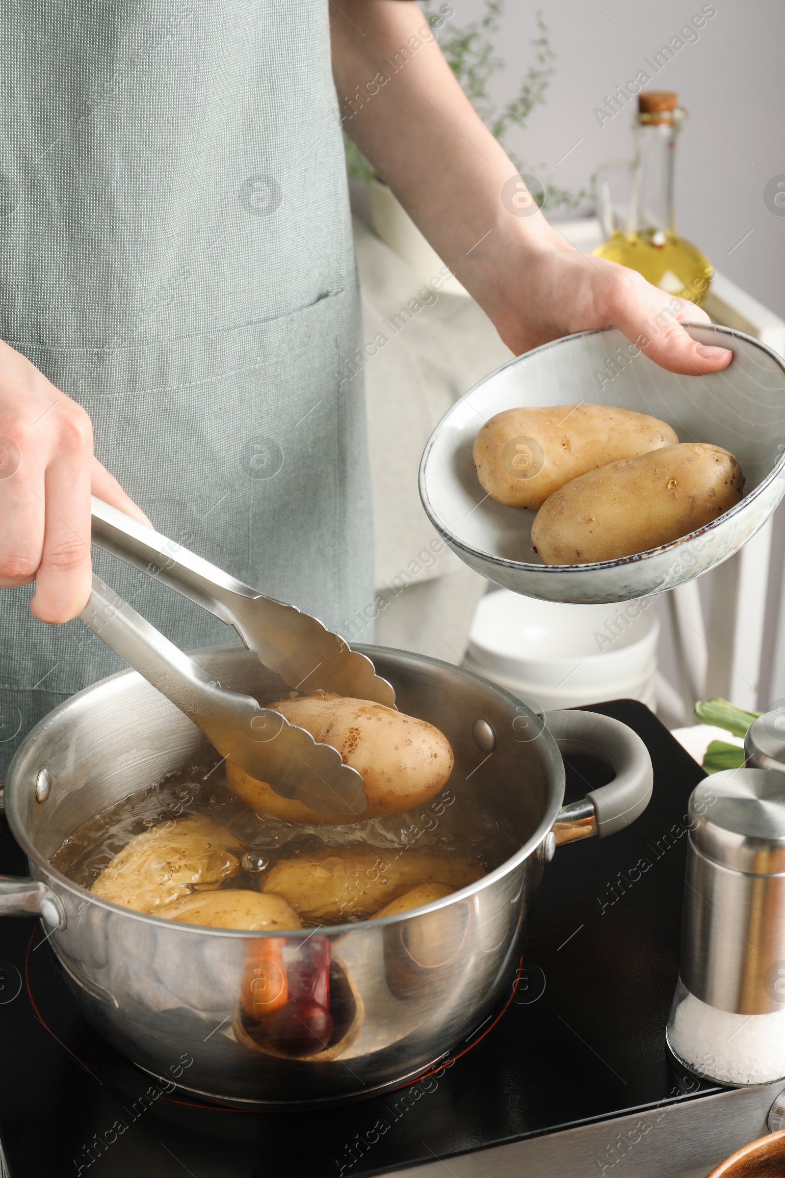 Photo of Woman putting raw potato into pot on stove, closeup