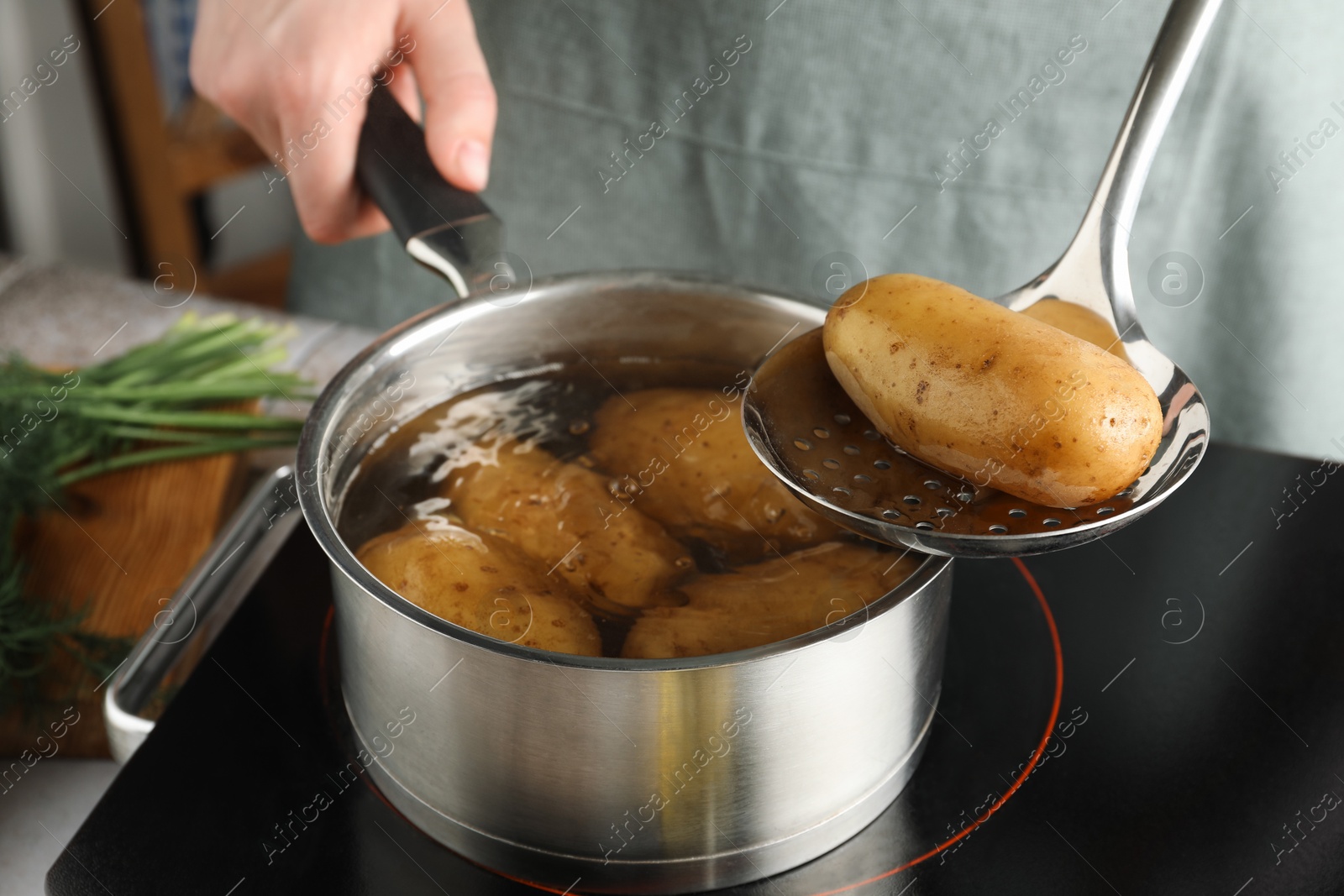 Photo of Woman taking boiled potato from saucepan on stove, closeup