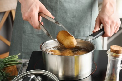 Woman taking boiled potato from saucepan on stove, closeup