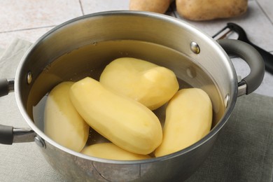 Photo of Raw potatoes in pot with water on table, closeup