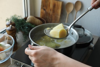 Woman taking boiled potato from pot on stove, closeup