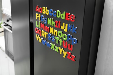 Photo of Alphabetical order. Many bright magnetic letters on fridge indoors