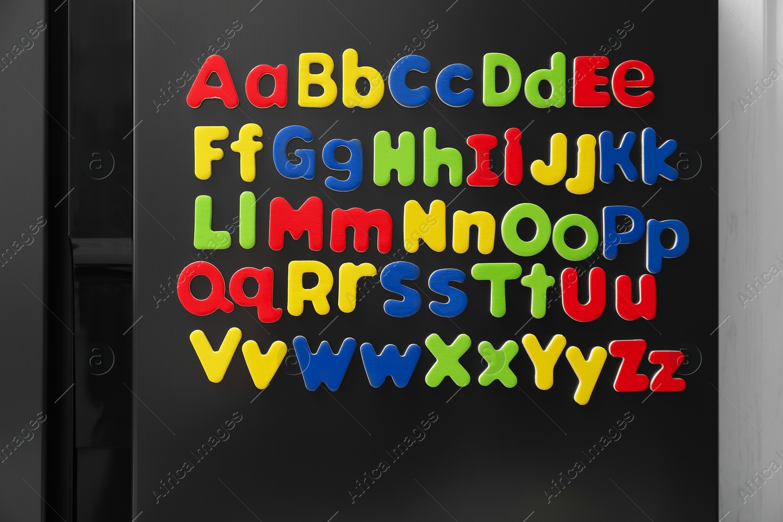 Photo of Alphabetical order. Many bright magnetic letters on fridge