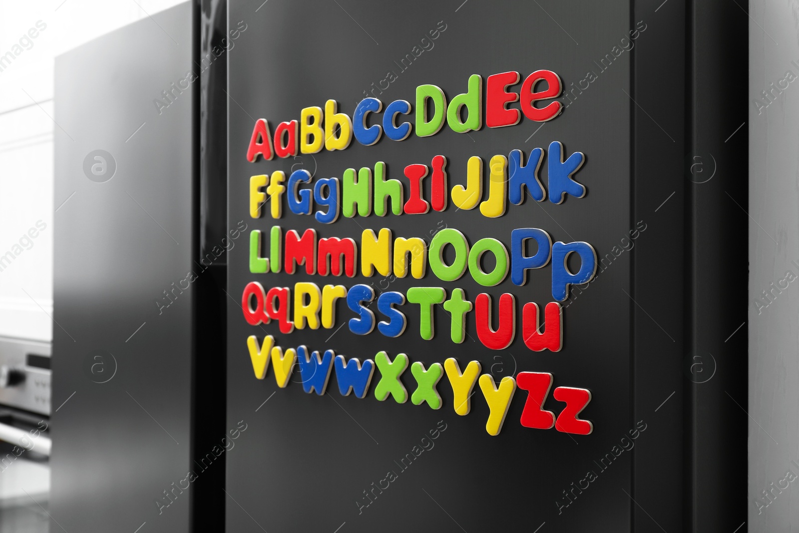 Photo of Alphabetical order. Many bright magnetic letters on fridge indoors