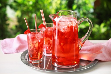 Photo of Tasty strawberry lemonade in jug and glasses on white table against blurred green background