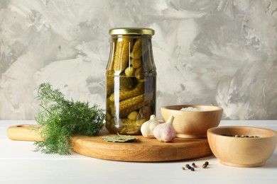 Pickled cucumbers in jar and spices on white table