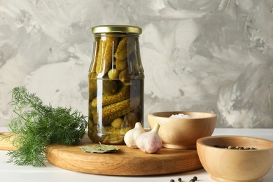 Pickled cucumbers in jar and spices on white table