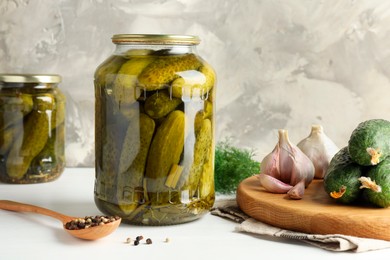 Pickles in jars, fresh cucumbers and spices on white table