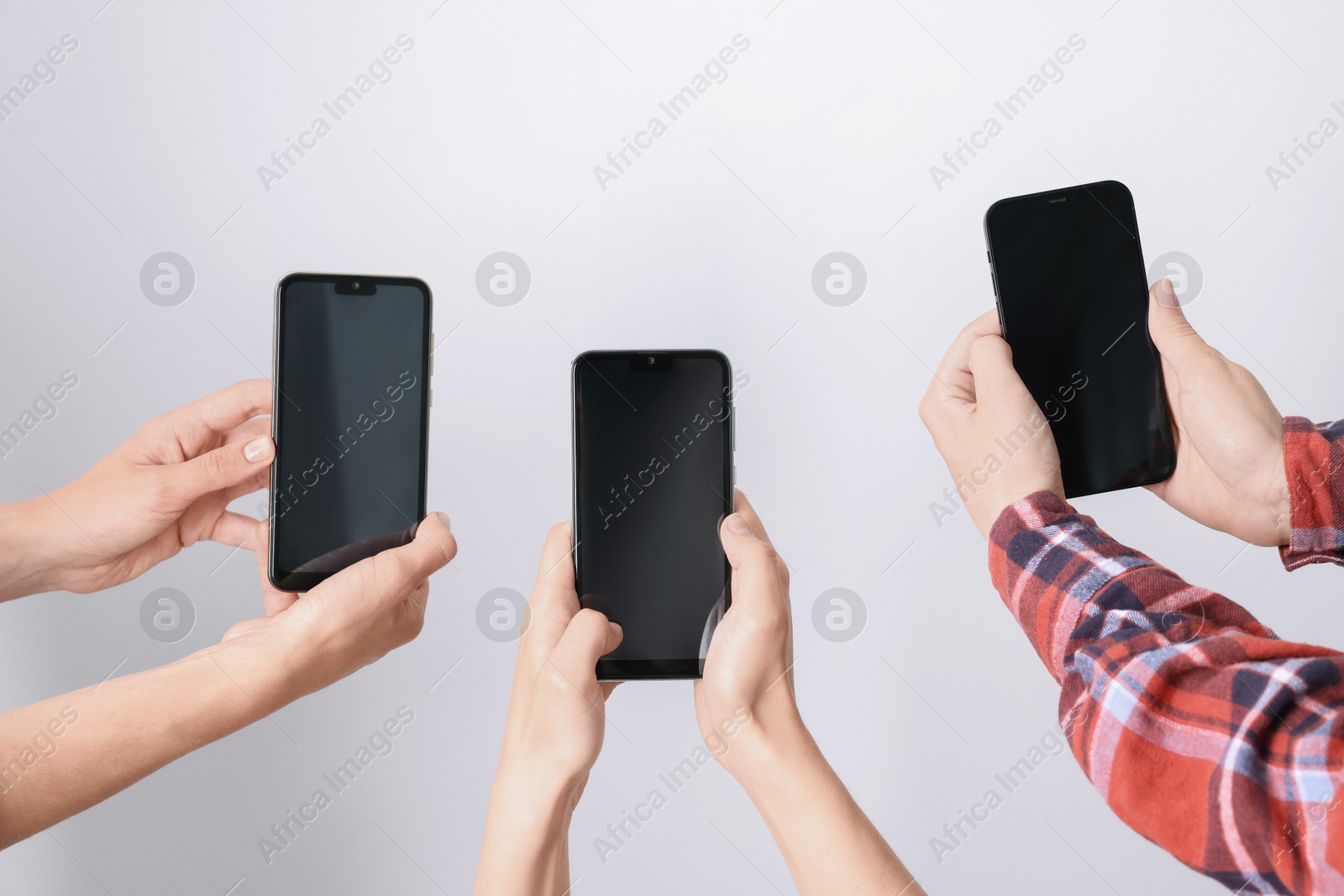 Photo of Women holding smartphones with blank screens against light grey background, closeup. Mockup for design