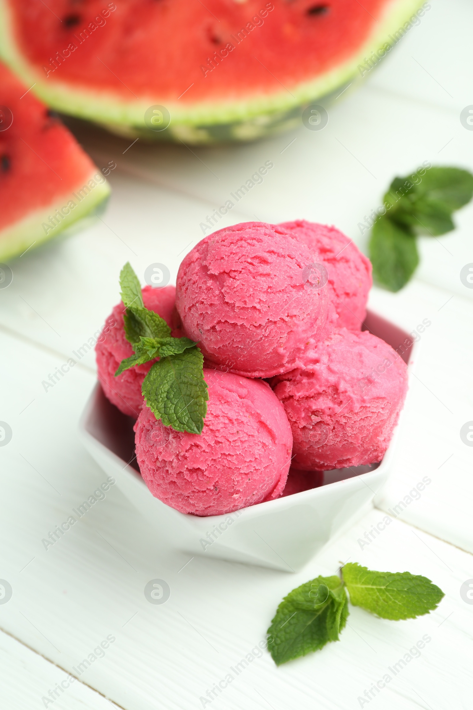 Photo of Scoops of tasty watermelon sorbet with mint in bowl on white wooden table