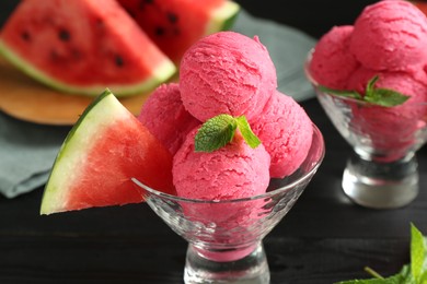 Photo of Scoops of tasty watermelon sorbet with mint in glass dessert bowls and fresh fruit on black table, closeup