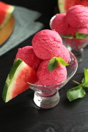 Photo of Scoops of tasty watermelon sorbet with mint in glass dessert bowls and fresh fruit on black table, closeup