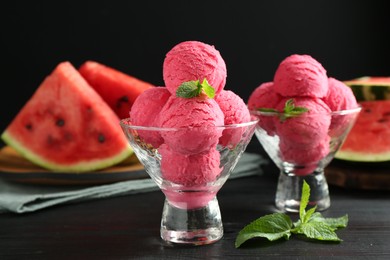 Photo of Scoops of tasty watermelon sorbet with mint in glass dessert bowls on black wooden table, closeup