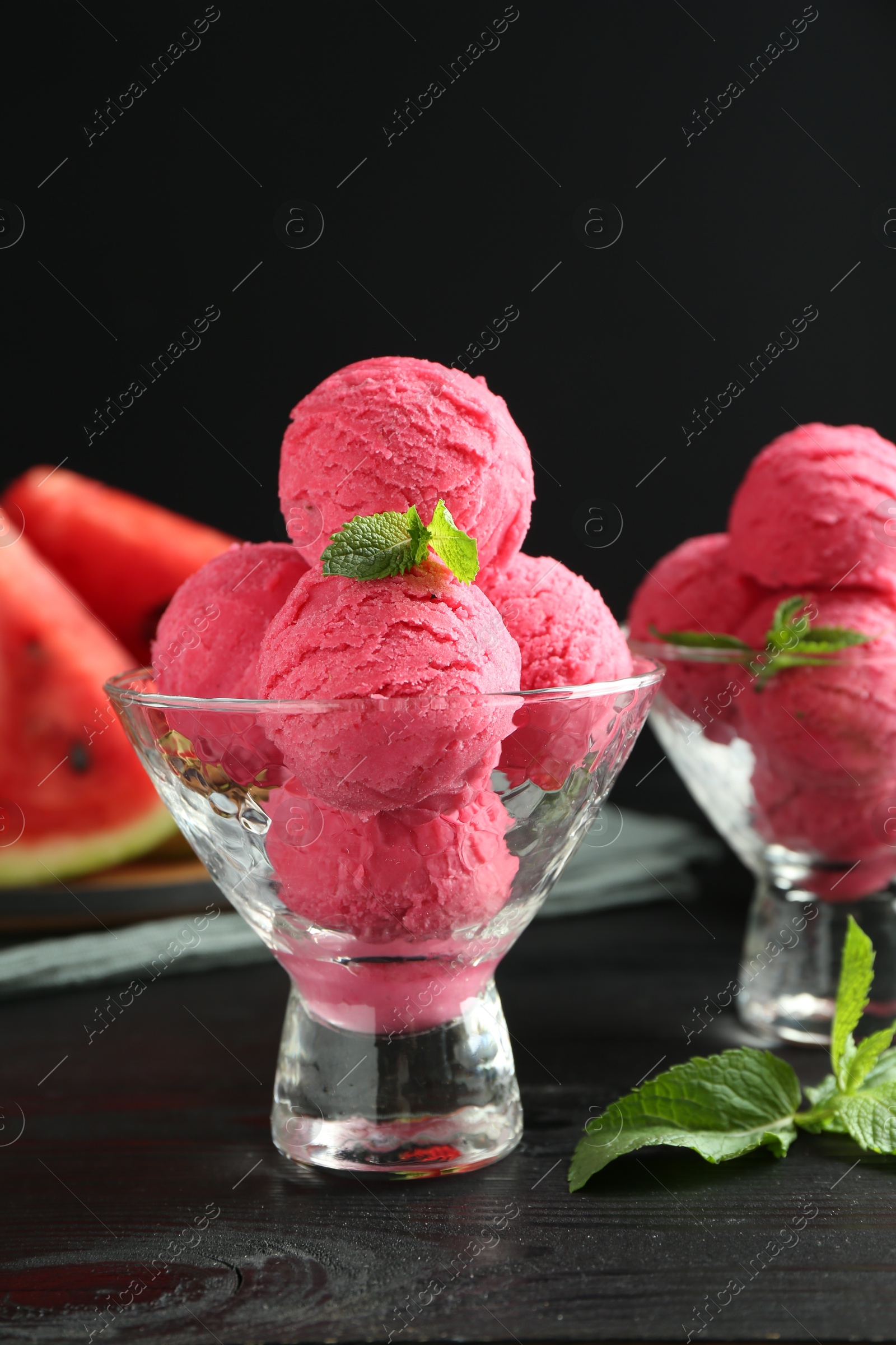 Photo of Scoops of tasty watermelon sorbet with mint in glass dessert bowls on black wooden table