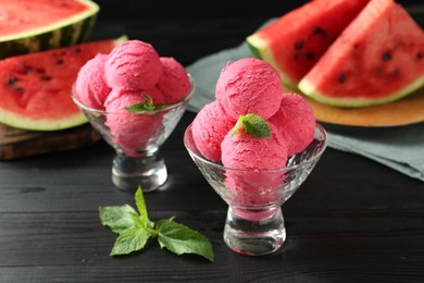 Photo of Scoops of tasty watermelon sorbet with mint in glass dessert bowls on black wooden table