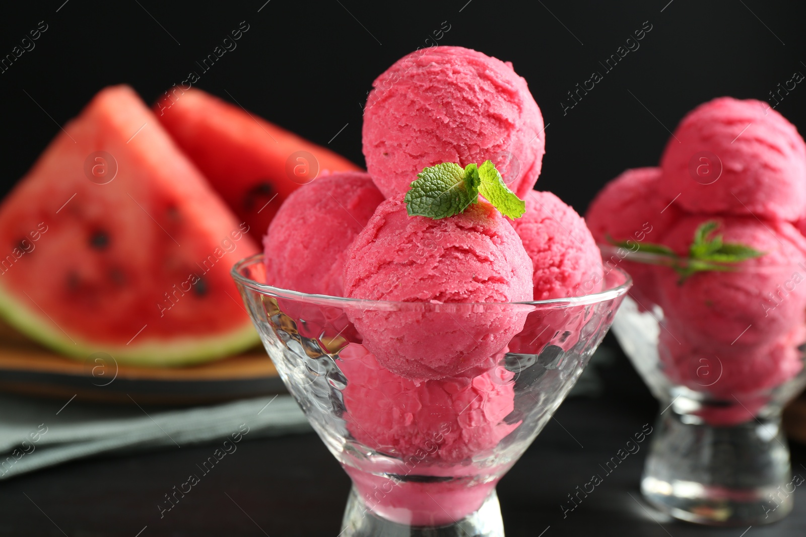 Photo of Scoops of tasty watermelon sorbet with mint in glass dessert bowls on black table, closeup