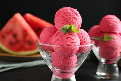 Photo of Scoops of tasty watermelon sorbet with mint in glass dessert bowls on black table, closeup