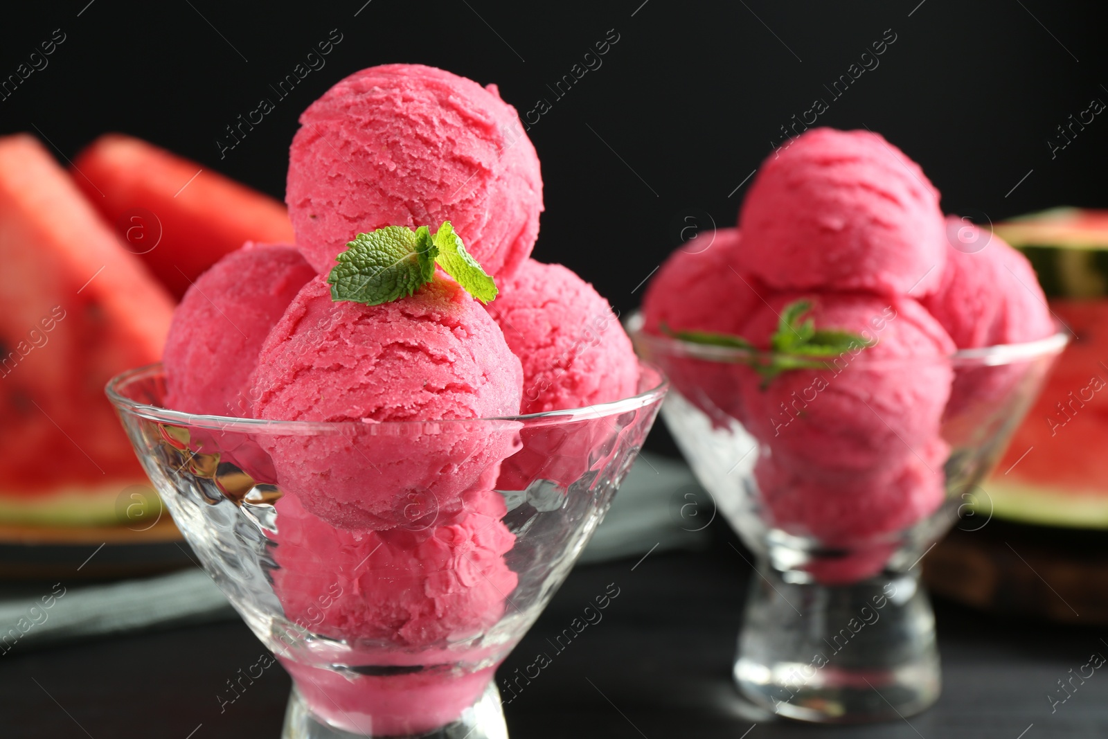 Photo of Scoops of tasty watermelon sorbet with mint in glass dessert bowls on black table, closeup