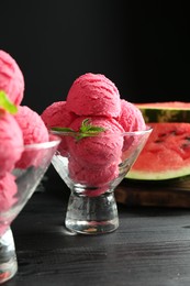 Photo of Scoops of tasty watermelon sorbet with mint in glass dessert bowls on black wooden table, closeup