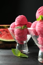 Photo of Scoops of tasty watermelon sorbet with mint in glass dessert bowls on black wooden table, closeup