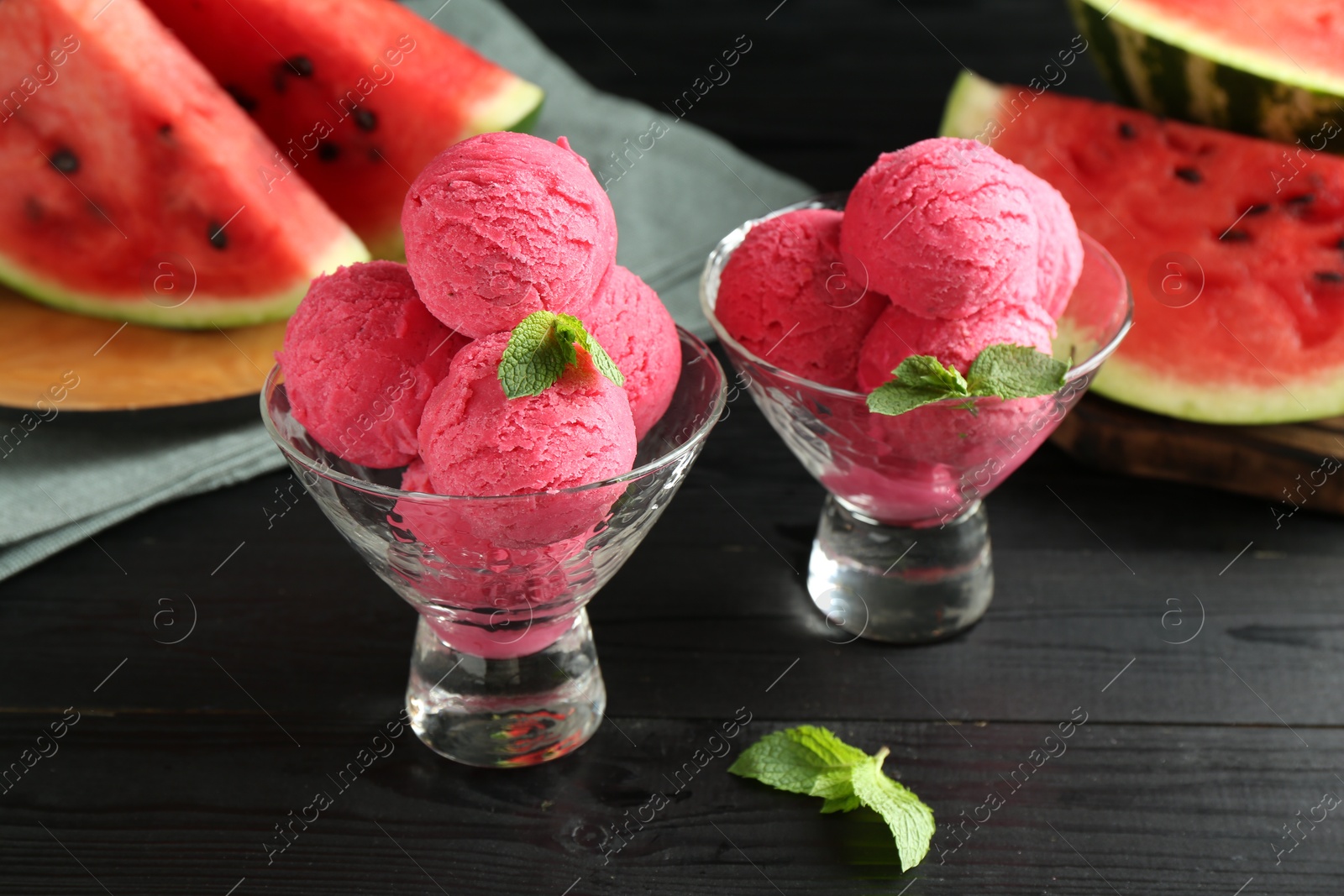 Photo of Scoops of tasty watermelon sorbet with mint in glass dessert bowls on black wooden table, closeup