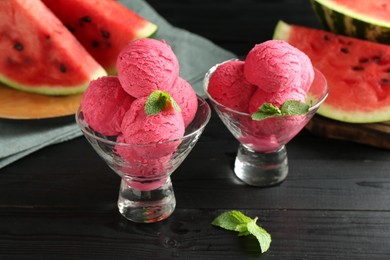 Scoops of tasty watermelon sorbet with mint in glass dessert bowls on black wooden table, closeup