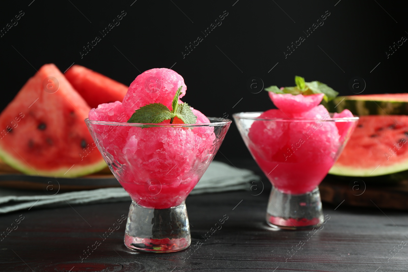 Photo of Tasty watermelon sorbet with mint in glass dessert bowls on black wooden table, closeup