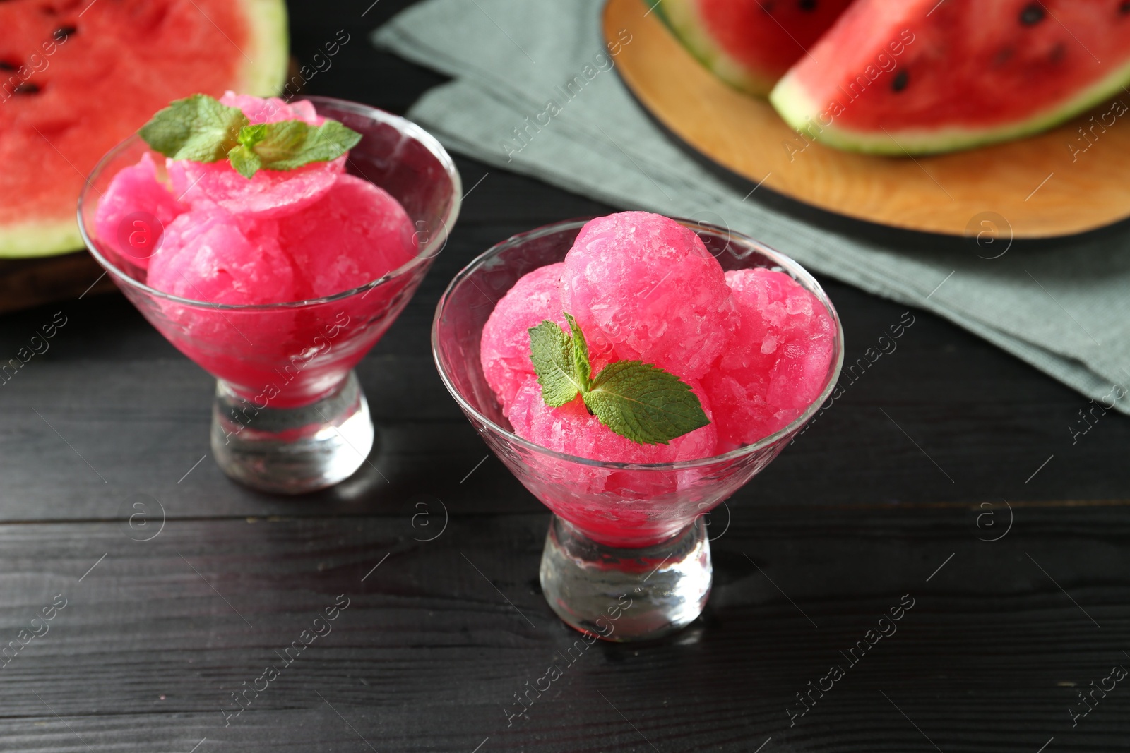 Photo of Tasty watermelon sorbet with mint in glass dessert bowls on black wooden table