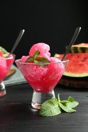 Photo of Tasty watermelon sorbet with mint in glass dessert bowls on black wooden table