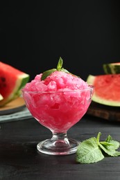 Photo of Tasty watermelon sorbet with mint in glass dessert bowl on black wooden table