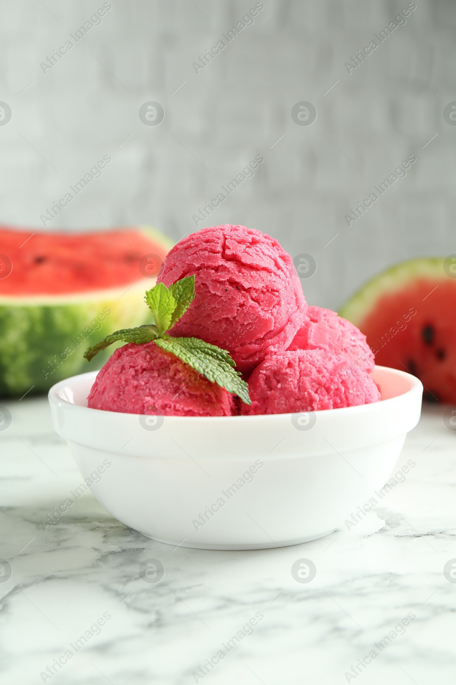 Photo of Scoops of tasty watermelon sorbet with mint in bowl on white marble table