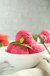 Photo of Scoops of tasty watermelon sorbet with mint in bowl and spoon on white marble table, closeup