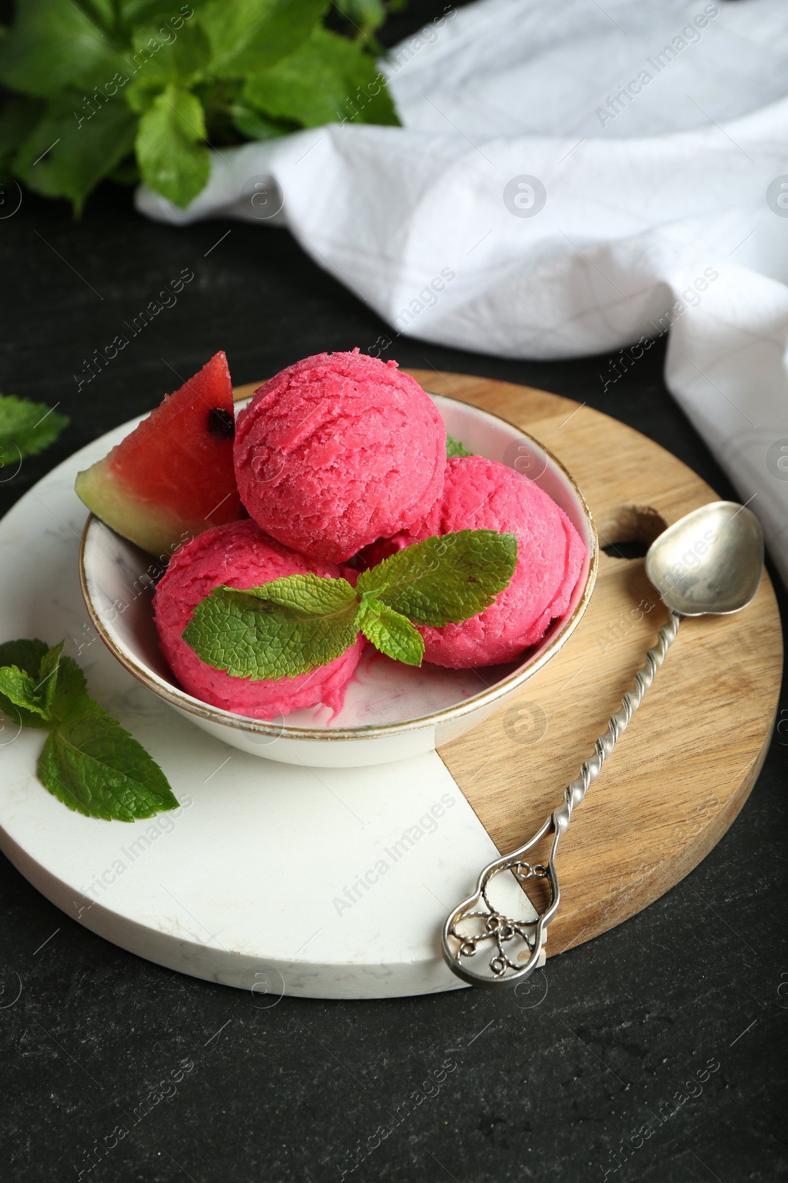 Photo of Scoops of tasty watermelon sorbet with mint, fresh fruit in bowl and spoon on grey textured table