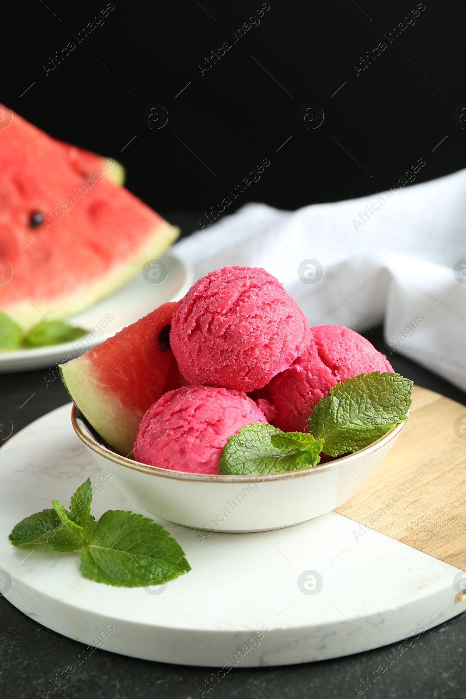 Photo of Scoops of tasty watermelon sorbet with mint and fresh fruit in bowl on grey textured table