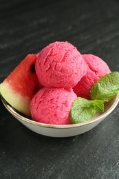 Photo of Scoops of tasty watermelon sorbet with mint and fresh fruit in bowl on grey textured table, closeup