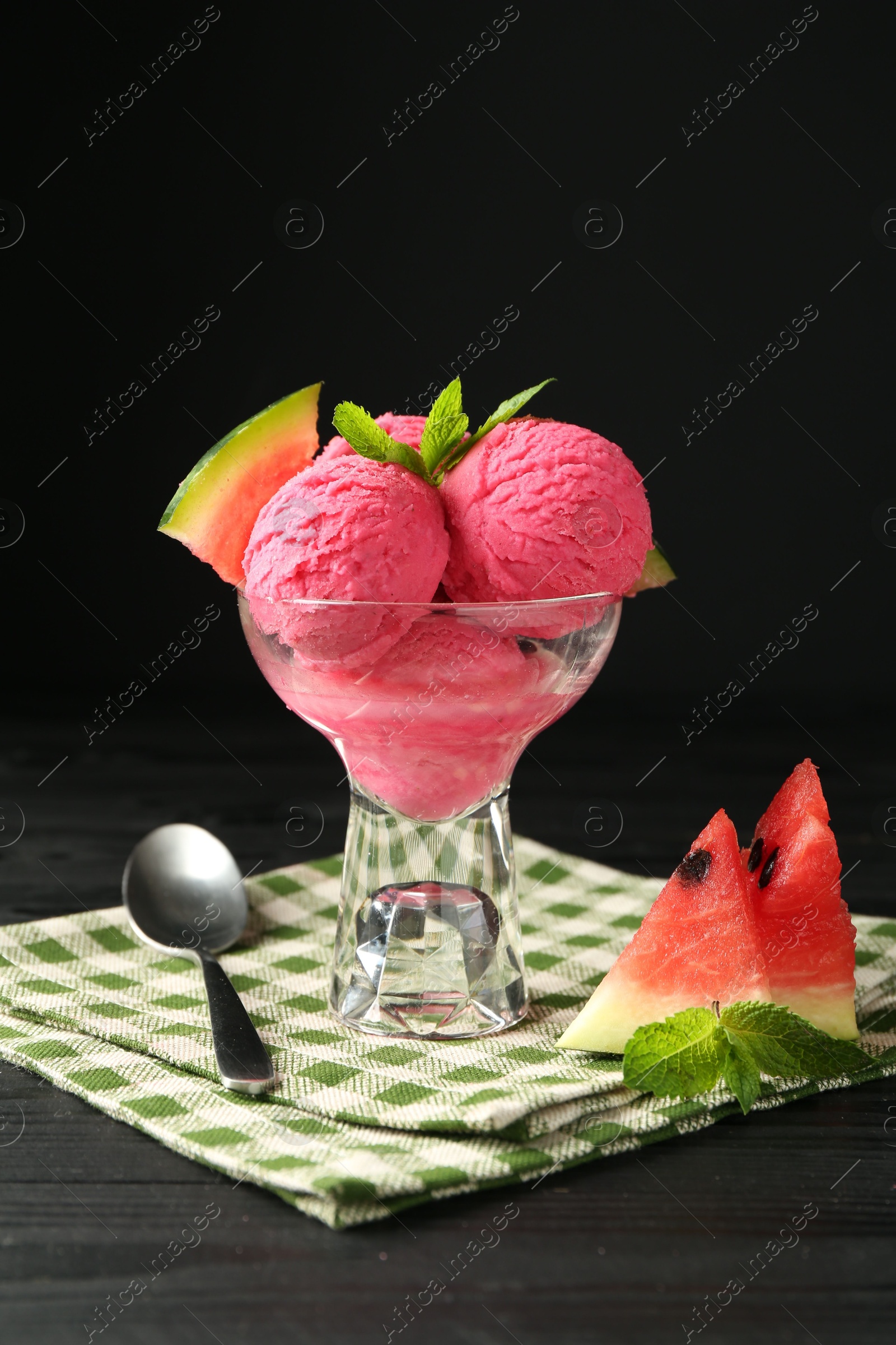 Photo of Scoops of tasty watermelon sorbet in glass dessert bowl with fresh fruit and spoon on black wooden table