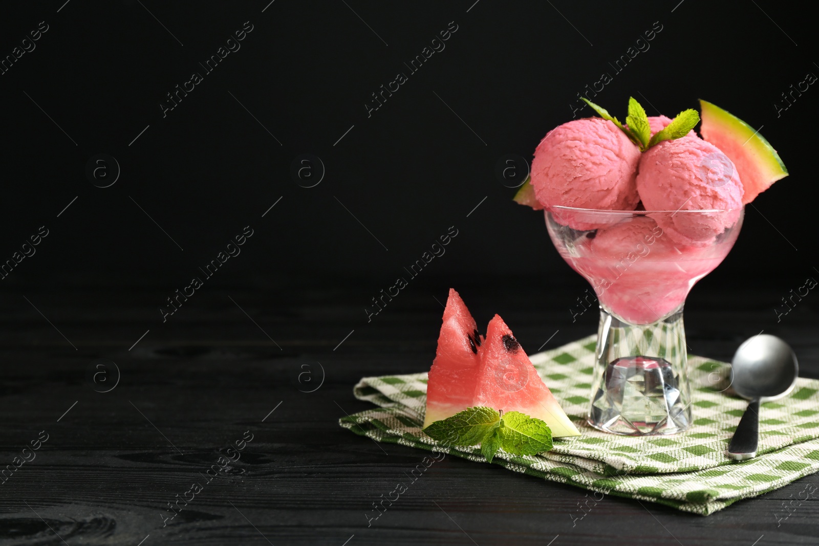 Photo of Scoops of tasty watermelon sorbet in glass dessert bowl with fresh fruit and spoon on black wooden table, space for text