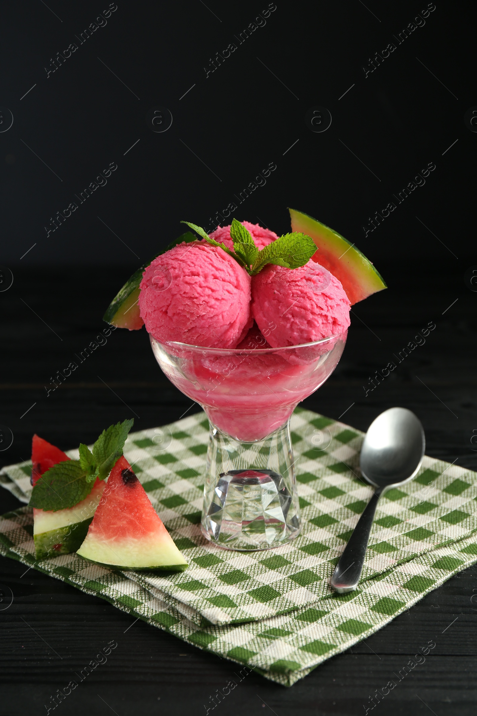 Photo of Scoops of tasty watermelon sorbet in glass dessert bowl with fresh fruit and spoon on black wooden table