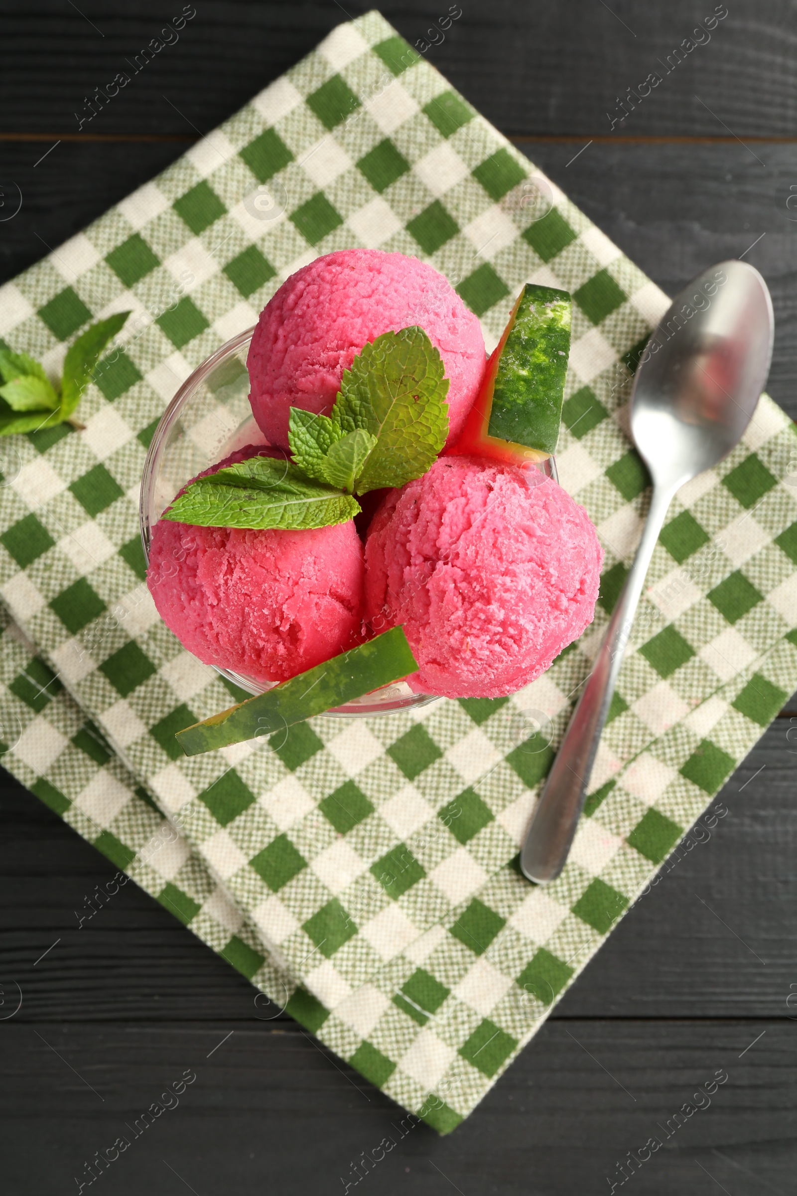 Photo of Scoops of tasty watermelon sorbet in glass dessert bowl with fresh fruit and spoon on black wooden table, flat lay