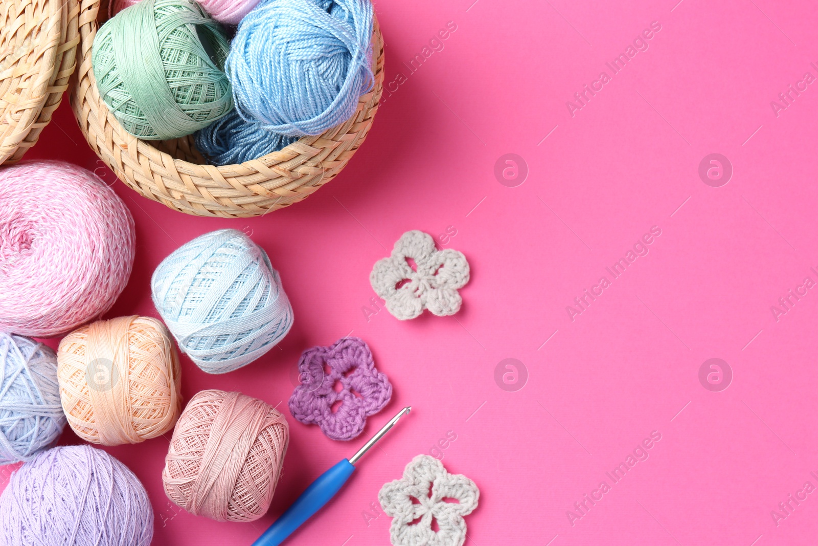 Photo of Different colorful yarns, crochet flowers and hook on pink background, flat lay. Space for text