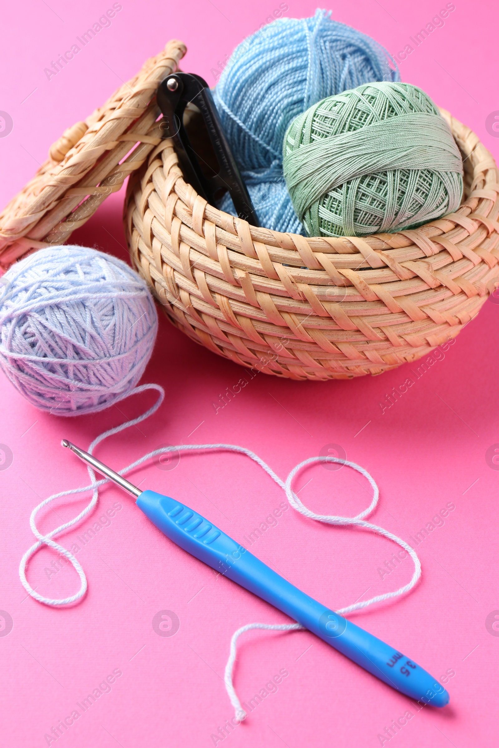 Photo of Different colorful yarns and crochet hook on pink background