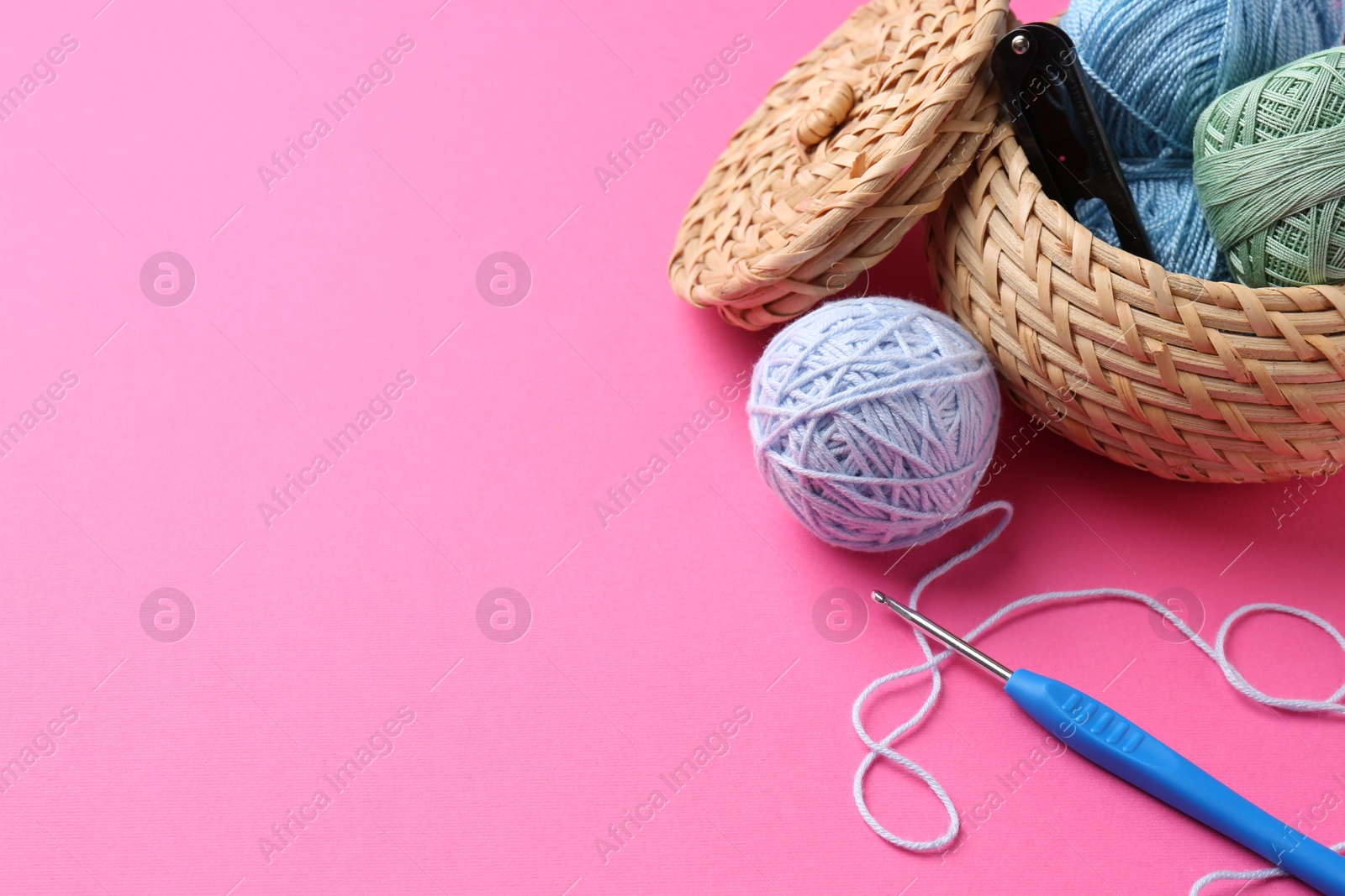 Photo of Different colorful yarns and crochet hook on pink background. Space for text