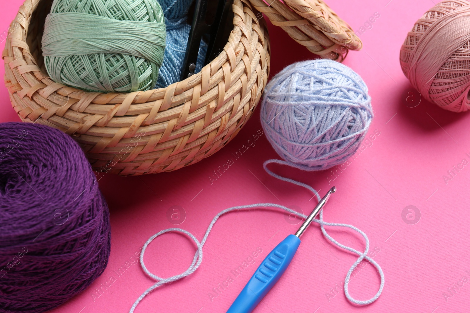 Photo of Different colorful yarns and crochet hook on pink background