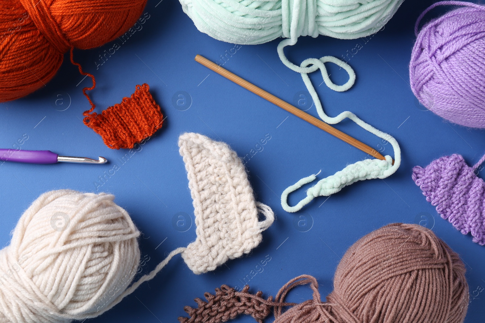 Photo of Different colorful yarns, pattern samples and crochet hook on blue background, flat lay