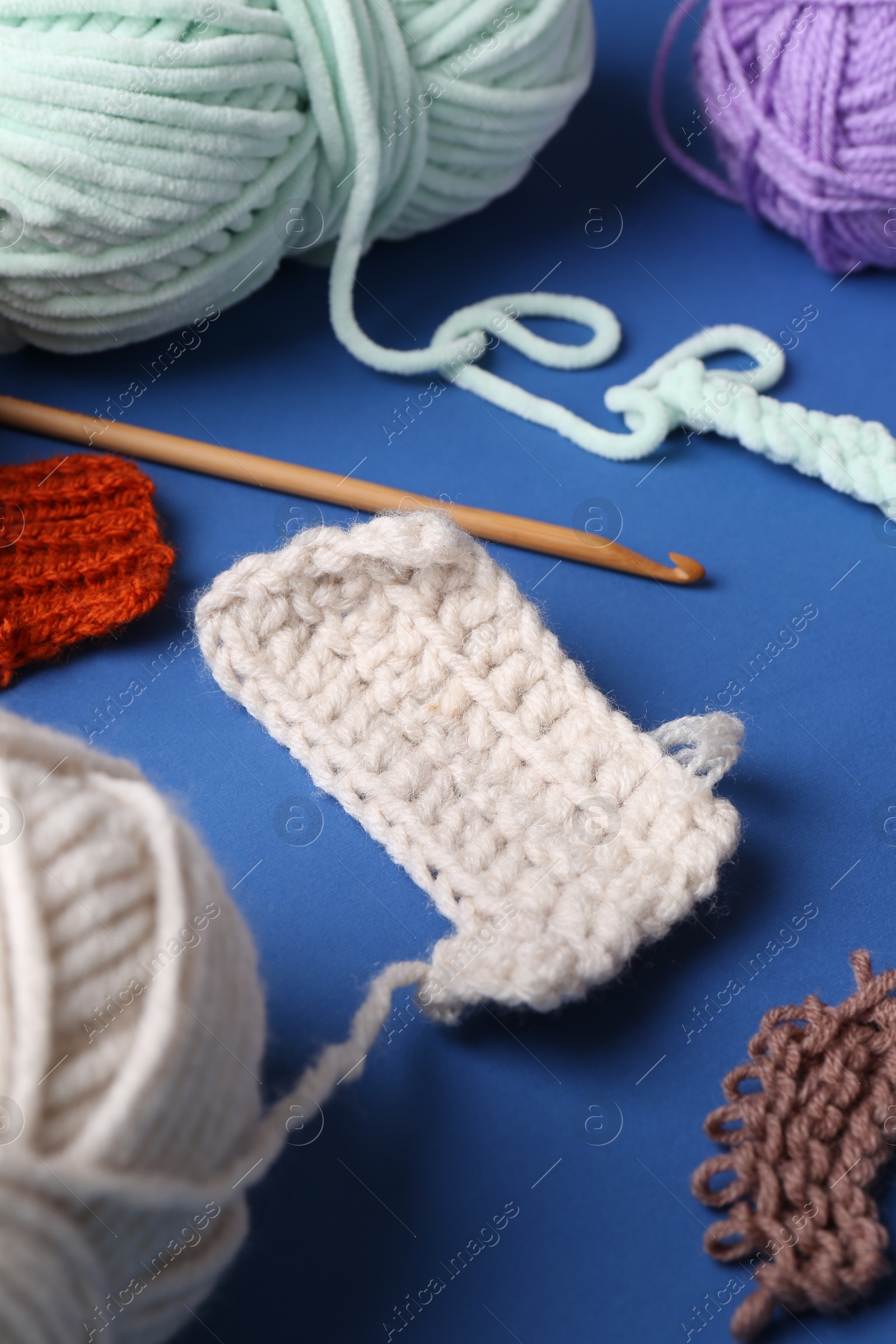 Photo of Different colorful yarns, pattern samples and crochet hook on blue background, closeup