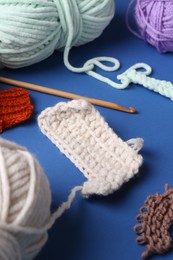 Photo of Different colorful yarns, pattern samples and crochet hook on blue background, closeup