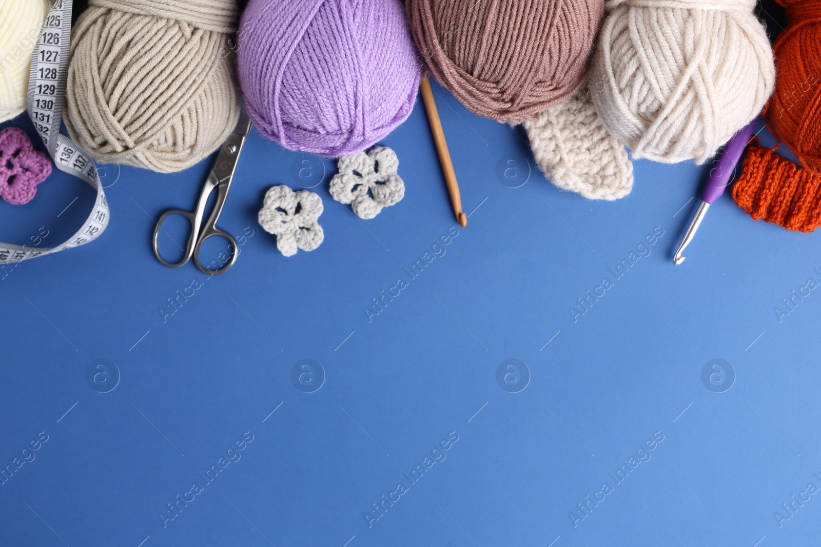 Photo of Different colorful yarns, crochet flowers, hooks and scissors on blue background, flat lay. Space for text