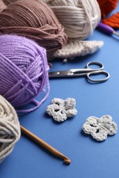 Photo of Different colorful yarns, crochet flowers, hook and scissors on blue background